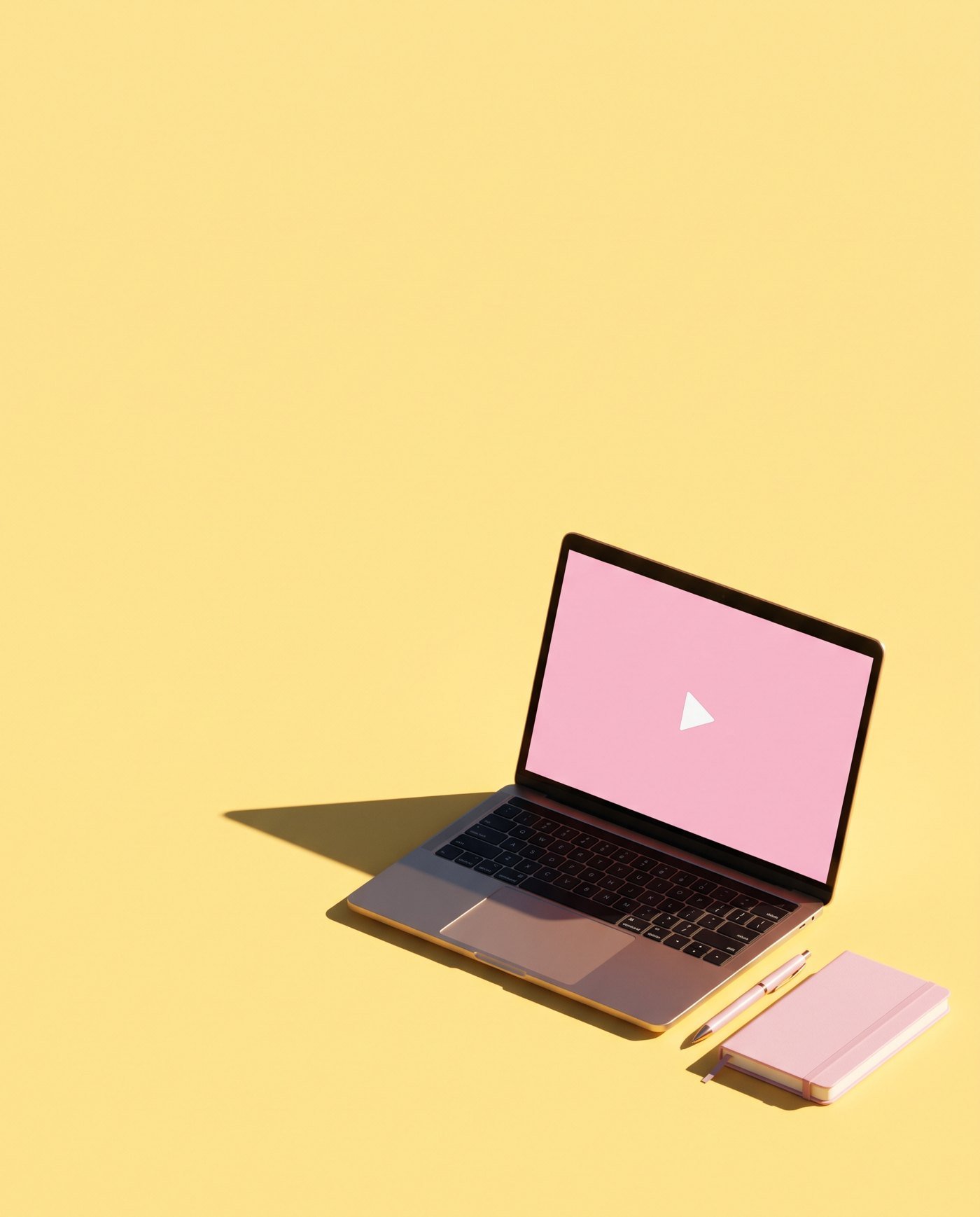 A laptop open on a kitchen table with a notebook and a pen